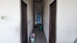 Um corredor estreito com duas portas de cada lado, uma porta azul no final, um relógio e uma lixeira verde.