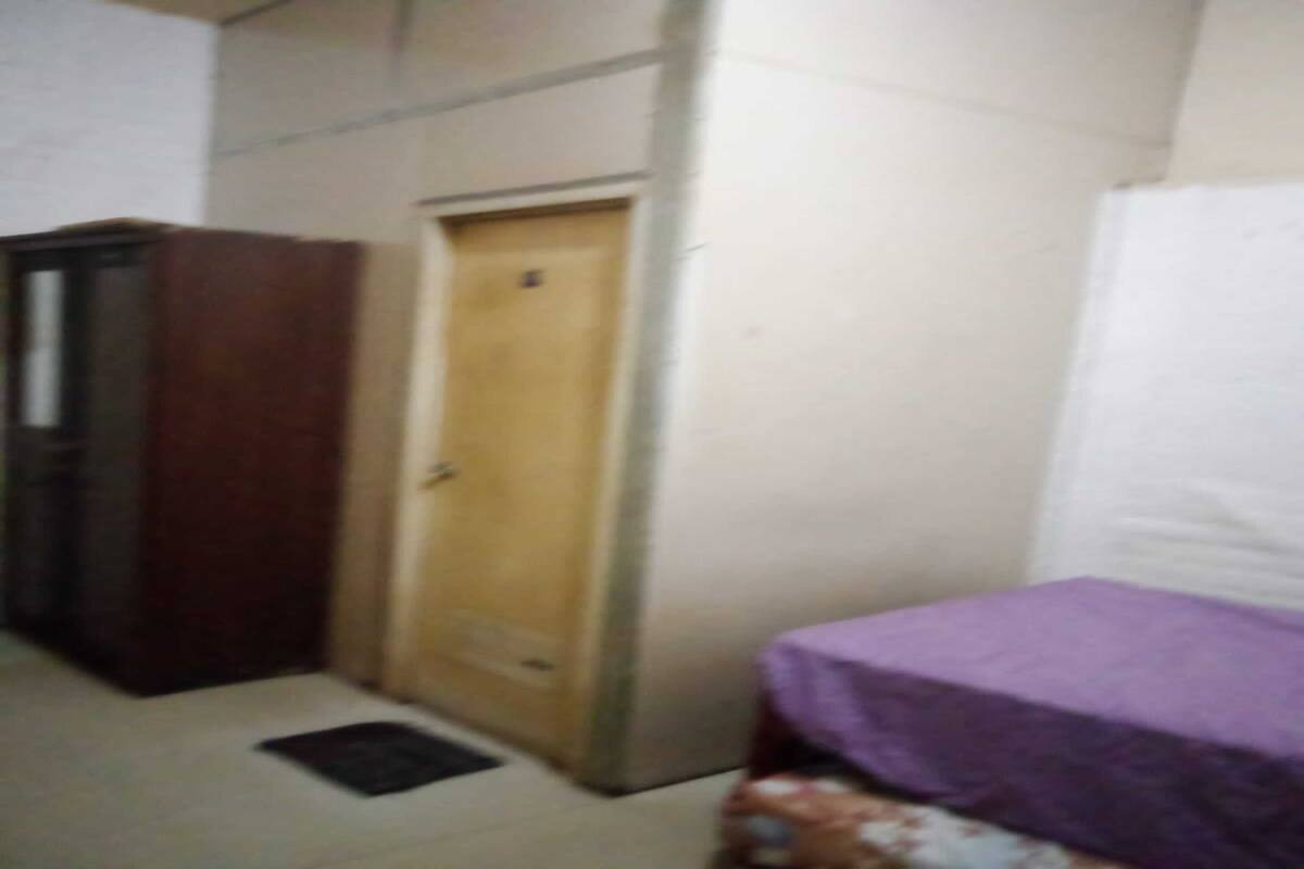 Een kleine kamer met een houten deur, een bed met een paarse spreidek en een betegelde vloer.