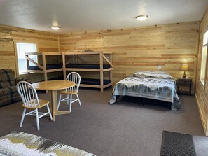 Una habitación tipo cabaña con literas, una mesa de comedor y una cama con una manta estampada.