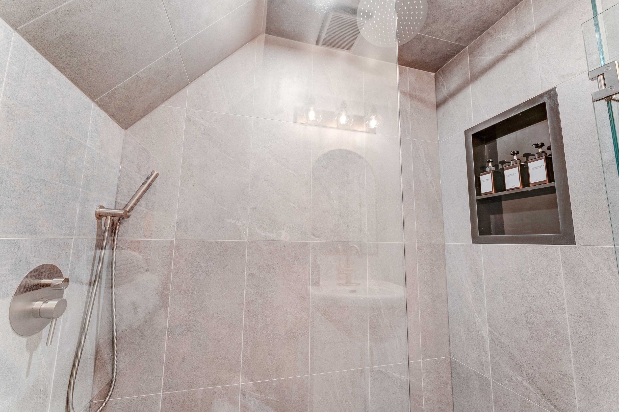 Een moderne badkamer met een douchecabine van glas, een ingebouwd wastafelmeubel en een plank met toiletartikelen.