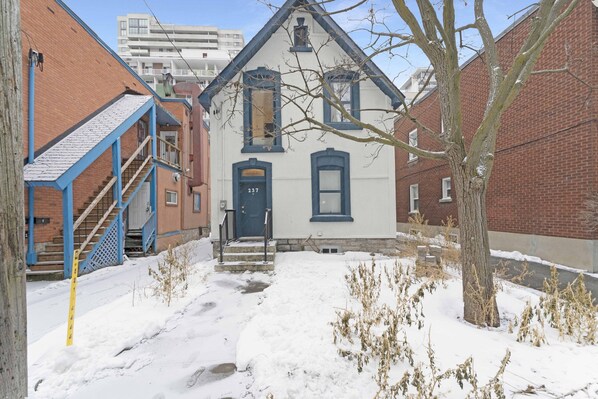 A snow-covered courtyard with a white building featuring a blue door and windows, surrounded by brick buildings.