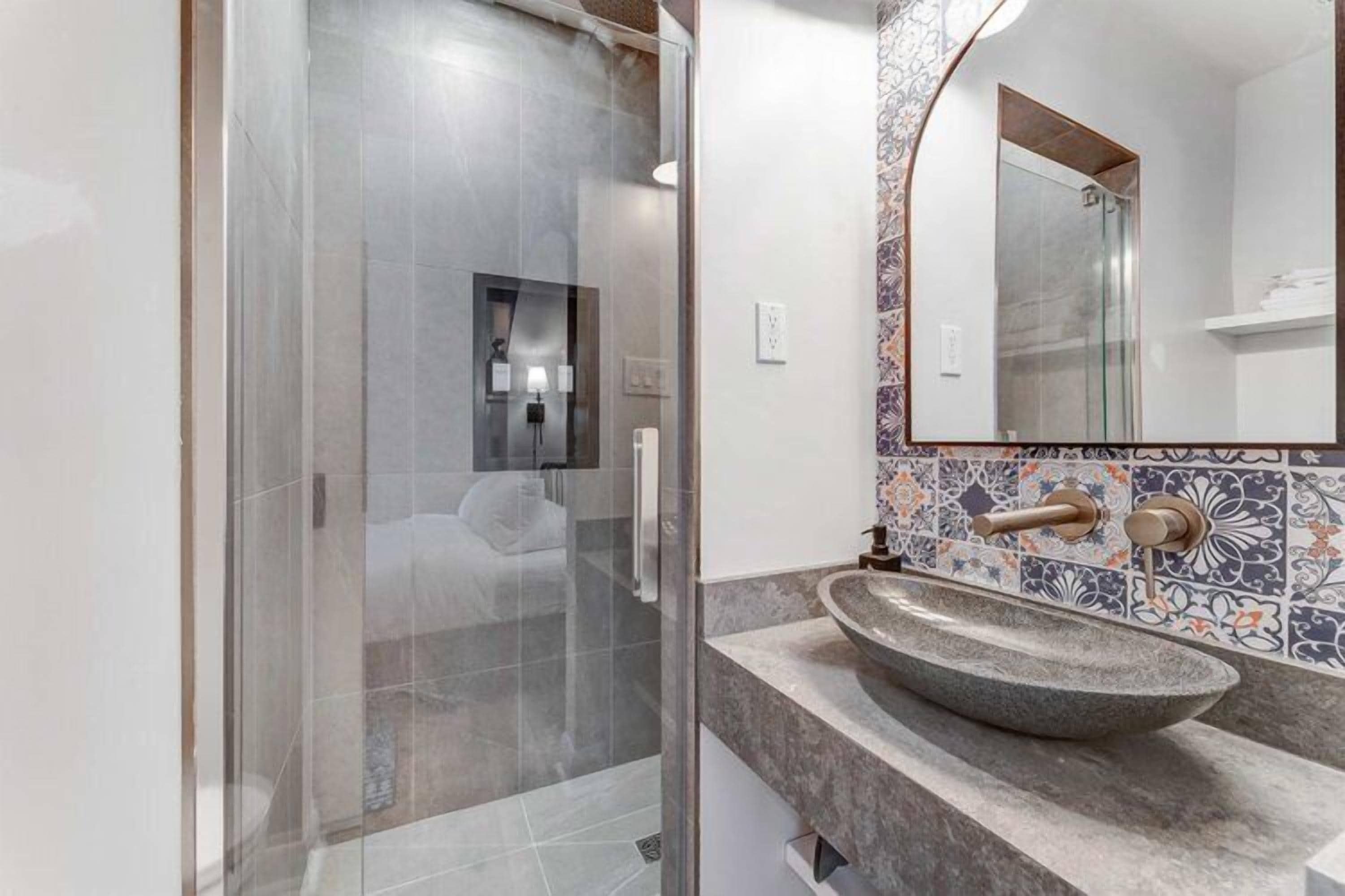 A modern bathroom with a glass shower enclosure, a large mirror, and a decorative tile backsplash.