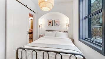 A bedroom with a bed, a window, and a hanging light fixture.
