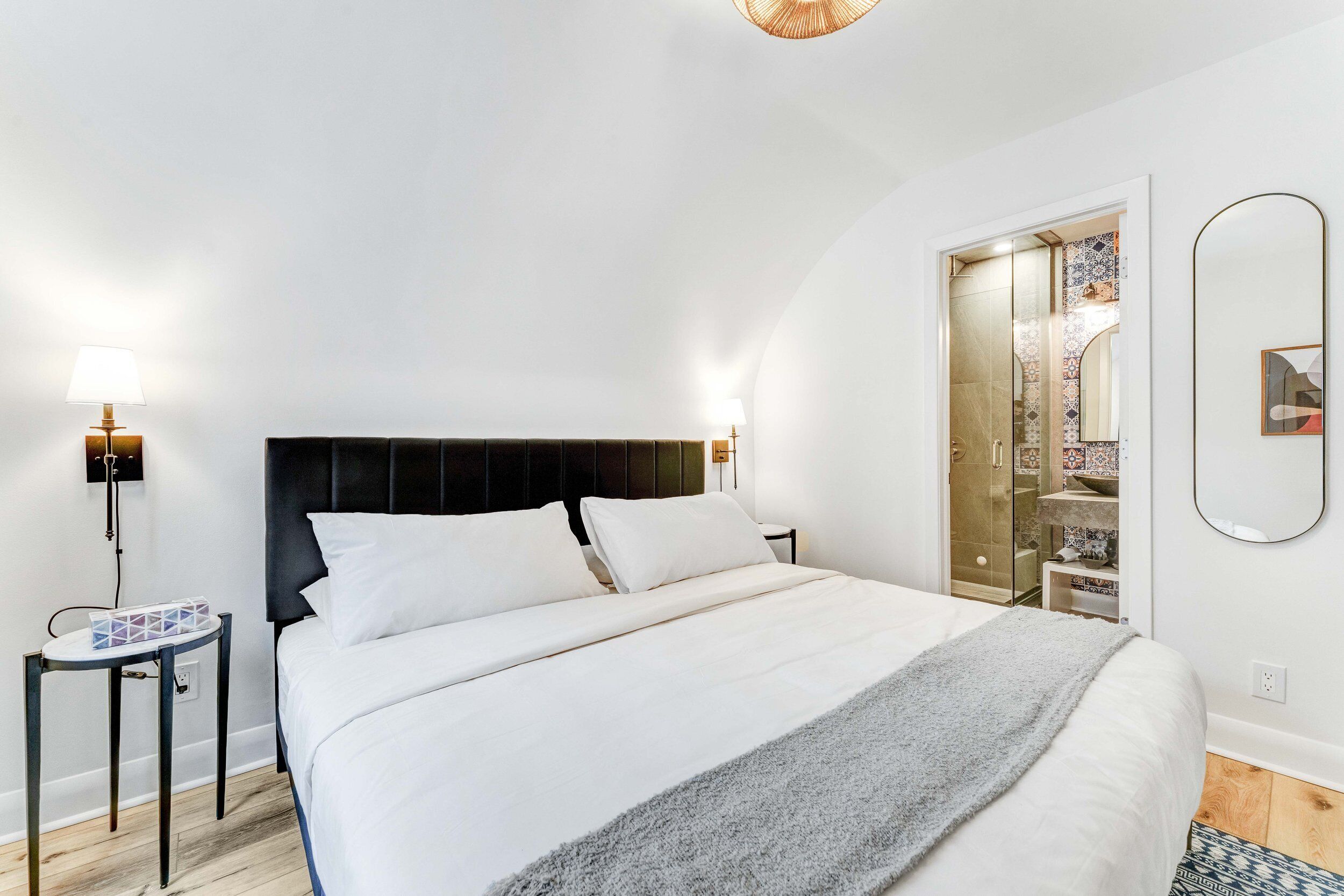 Een moderne slaapkamer met een groot bed, nachtkastjes, een spiegel en een inloopkast.