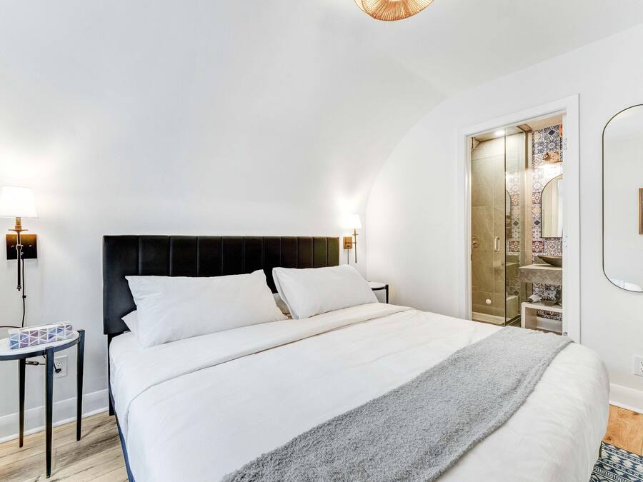 Een moderne slaapkamer met een groot bed, nachtkastjes, een spiegel en een inloopkast.