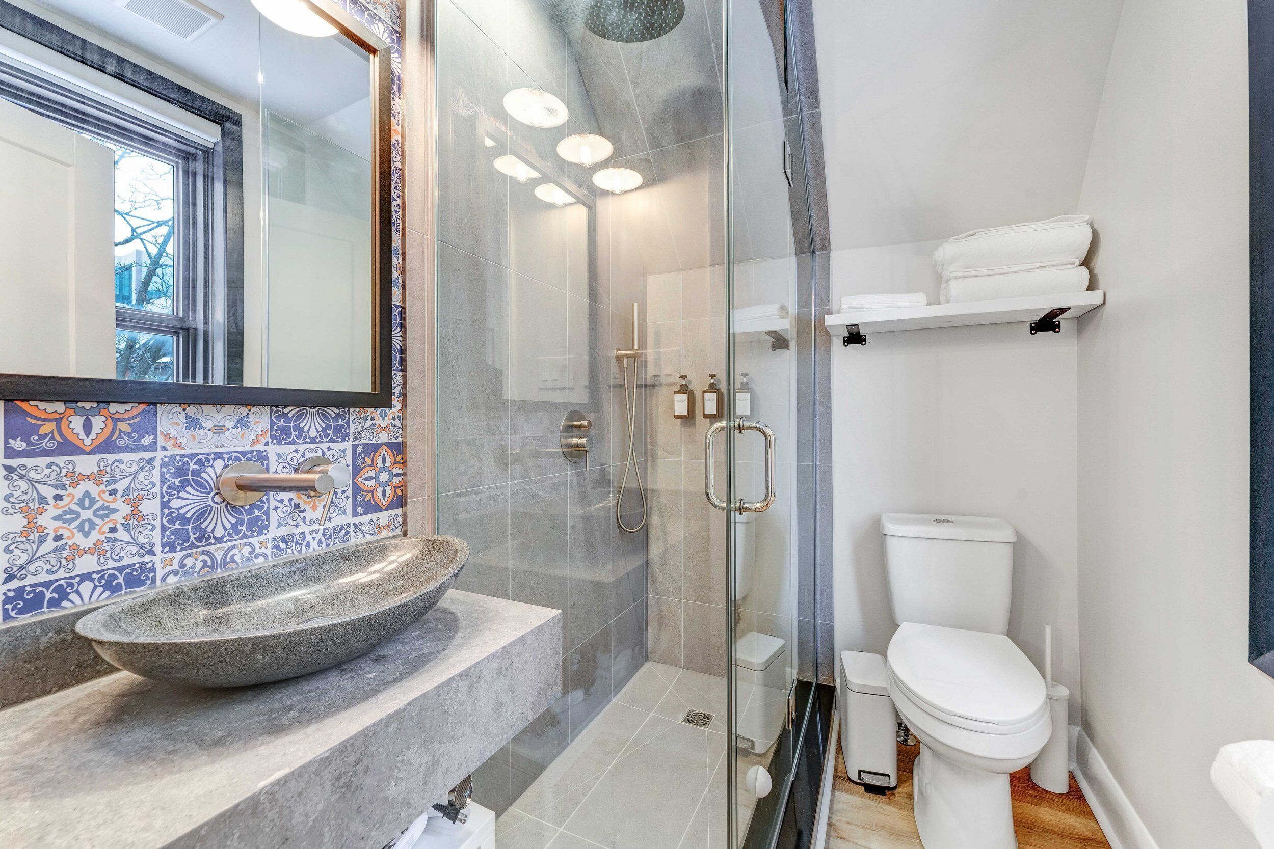 A modern bathroom with a glass-enclosed shower, a stone sink, and a white toilet.