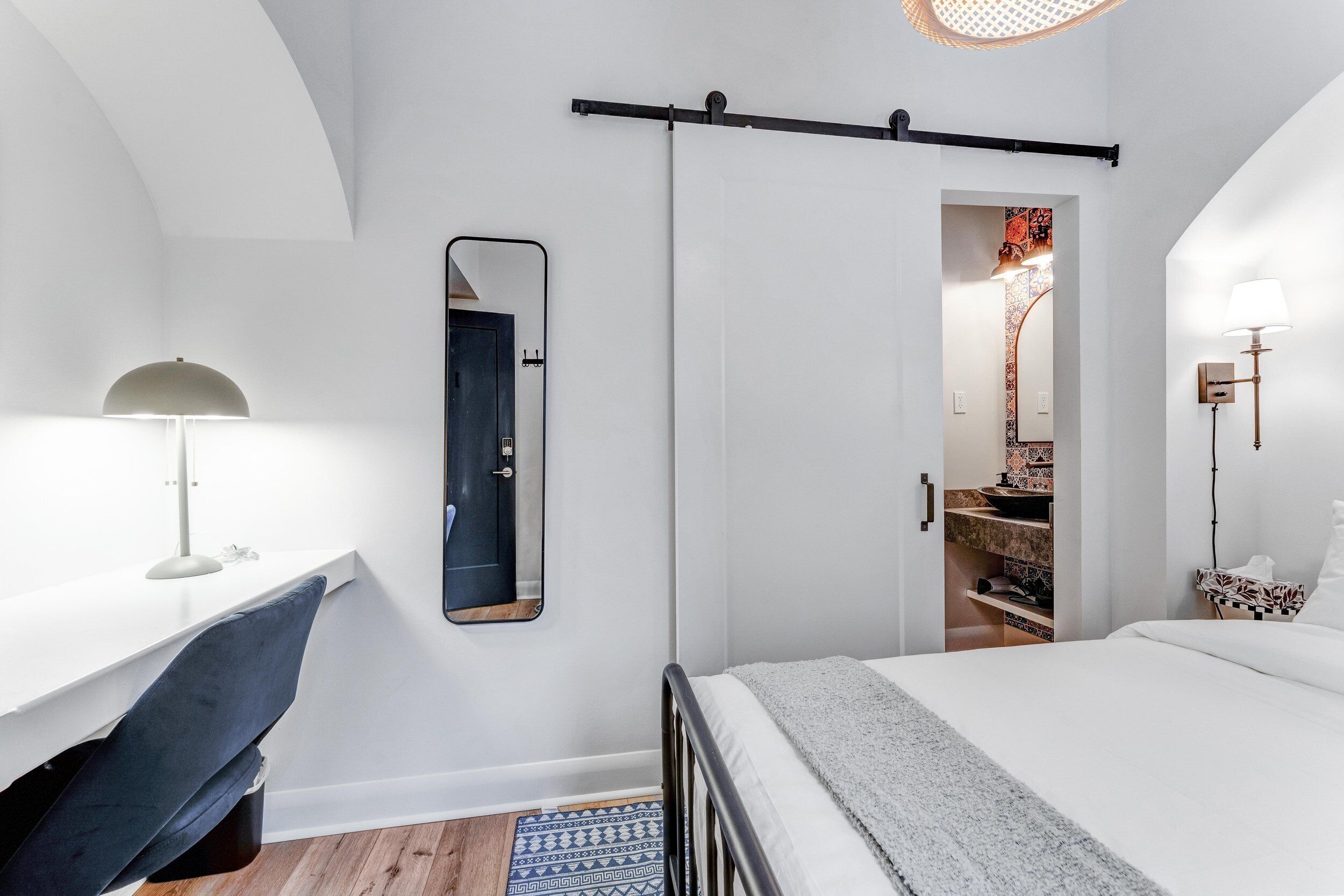 A bedroom with a bed, a desk with a chair, a mirror, and a wardrobe.
