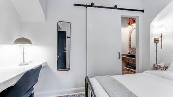 A bedroom with a bed, a desk with a chair, a mirror, and a wardrobe.