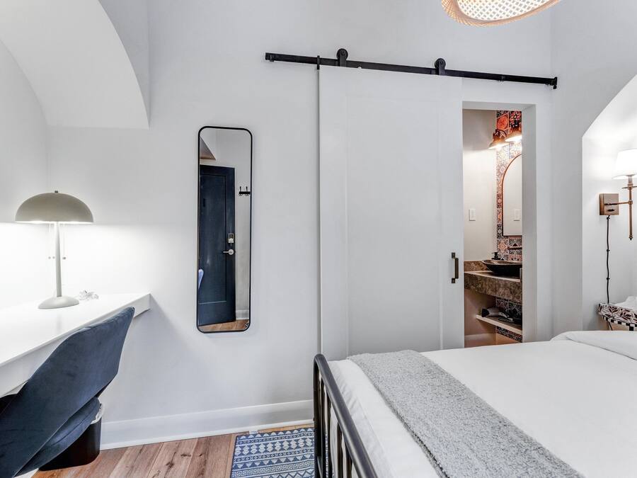A bedroom with a bed, a desk with a chair, a mirror, and a wardrobe.