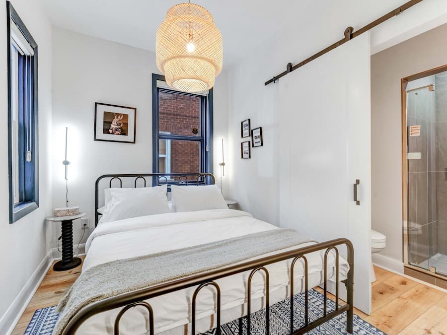 A bedroom with a bed, bedside table, lamp, and a hanging light fixture.