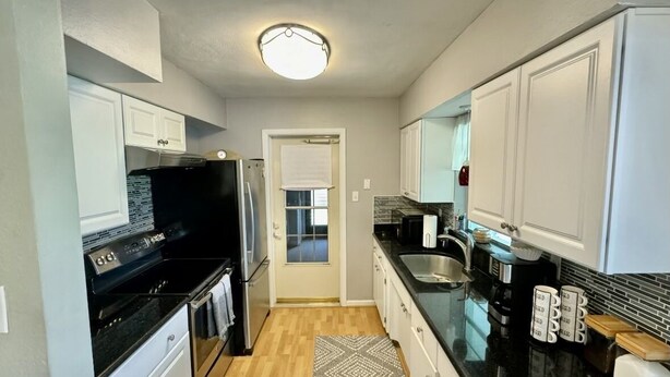 A compact kitchen with white cabinets, a black countertop, a stainless steel sink, and a built-in oven. - The Teal Turtle  (Seminole)