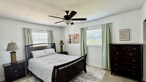 A bedroom with a bed, nightstands, a dresser, a ceiling fan, and a window with curtains. - The Teal Turtle  (Seminole)