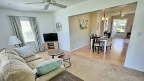 A living room with a sofa, coffee table, TV, and dining area with chairs and a table. - The Teal Turtle  (Seminole)