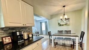 A kitchen with white cabinets, a black countertop, and a dining area with a table and chairs. - The Teal Turtle  (Seminole)