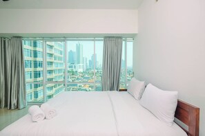 A hotel room with a large bed, two pillows, and a view of a cityscape through floor-to-ceiling windows. - Homey And Warm 1Br Apartment At Ambassade Kuningan (Jakarta)