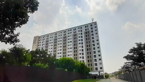 Un edificio residenziale alto con numerosi piani, circondato dal verde e da una recinzione.