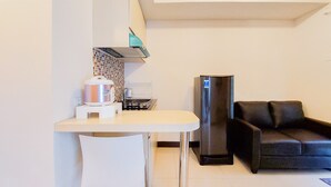 Una cucina compatta con un piano di lavoro bianco, un bollitore in acciaio inossidabile, un frigorifero nero e un divano in pelle nera.