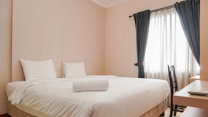 Een net opgemaakt bed met witte lakens, een houten nachtkastje en een stoel.