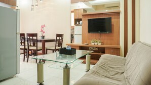 Een moderne woonkamer met een glazen salontafel, een beige bank, houten kasten en een flatscreen televisie aan de muur.