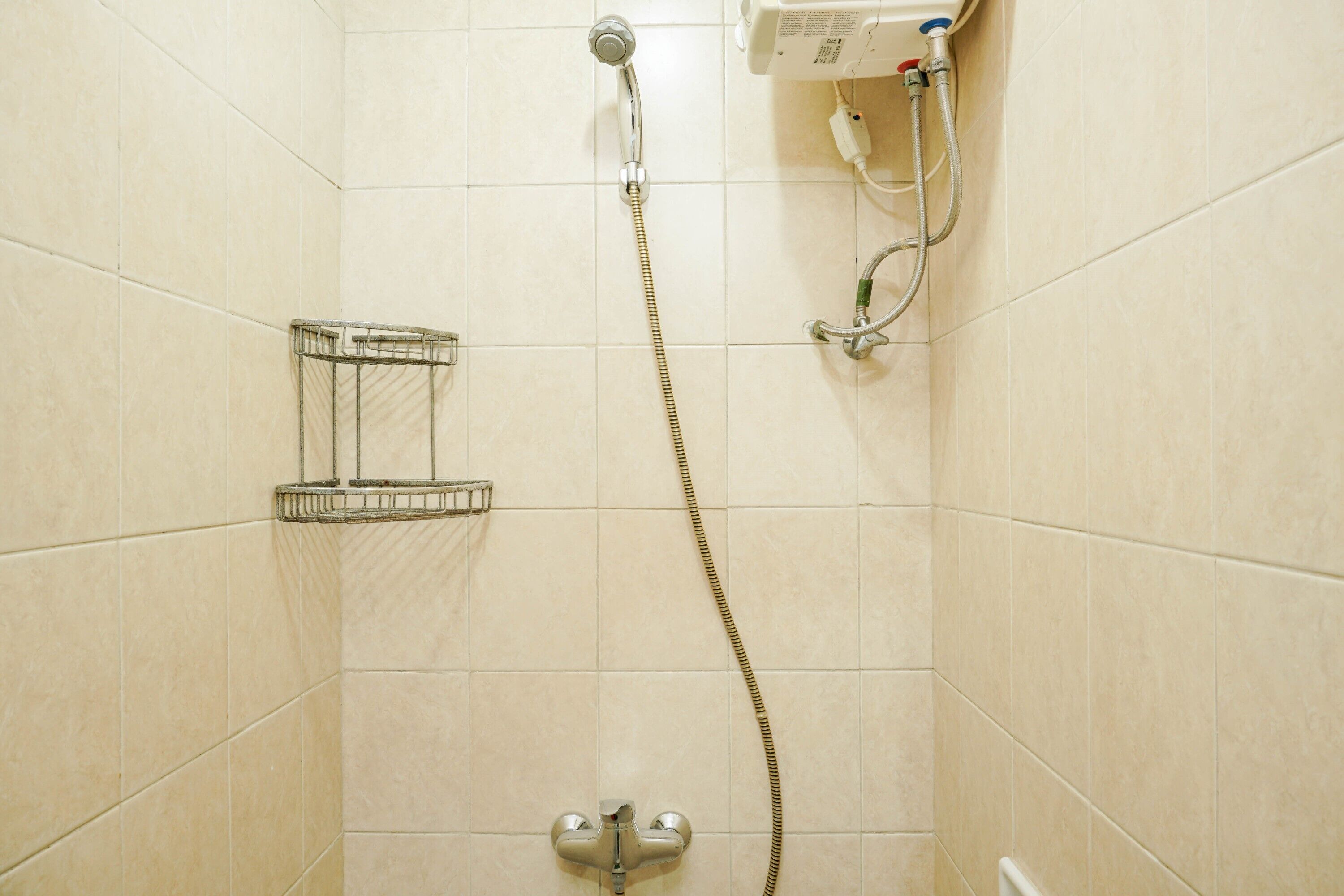 Ducha con cabezal de ducha de mano y grifo empotrado en la pared, barra para toallas y un enchufe en la pared.