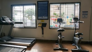 Een sportschool met loopbanden en hometrainers, grote ramen met metalen tralies, en een poster aan de muur.