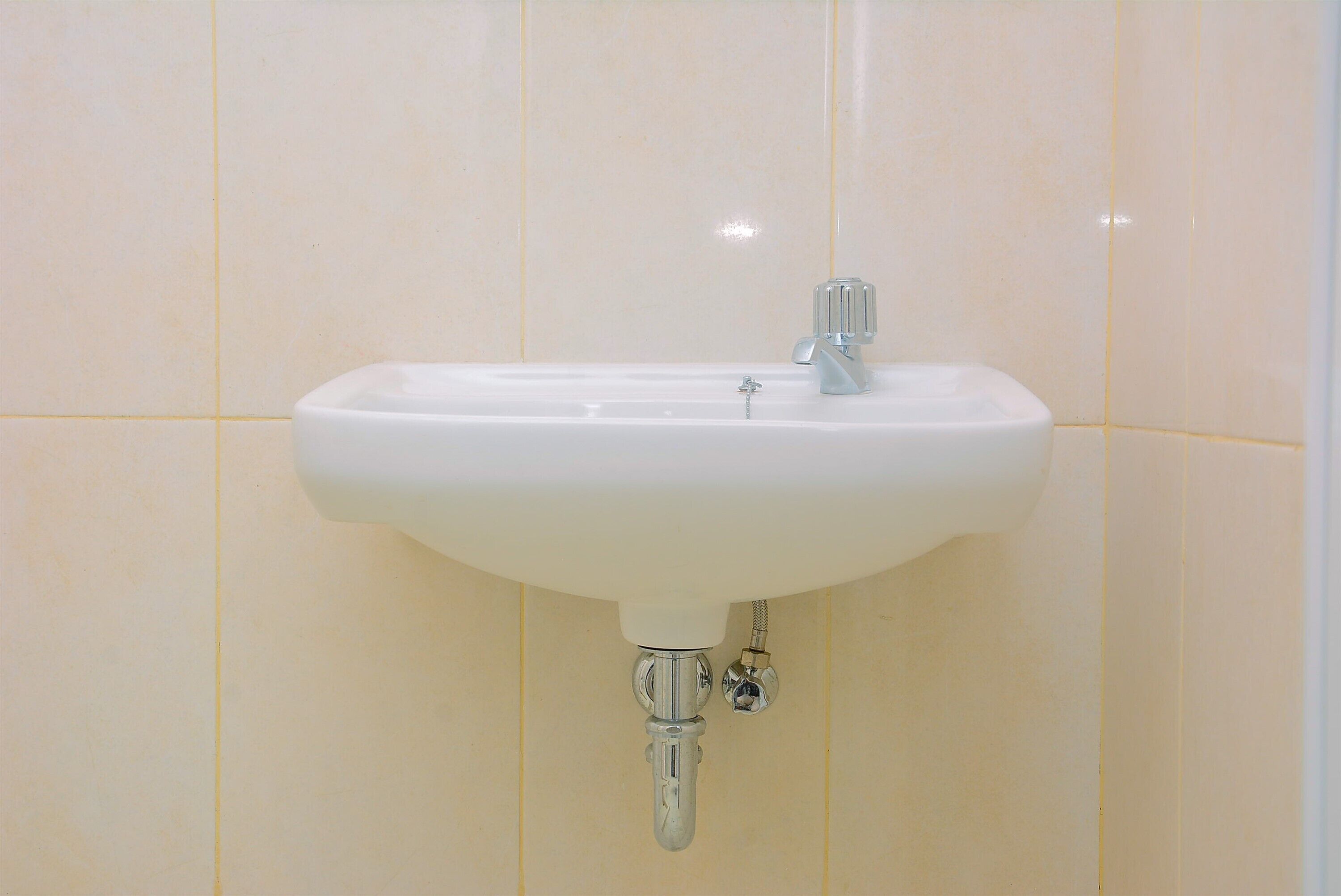 Ein weißes Waschbecken mit chromfarbenem Wasserhahn und einem S-förmigen Ablaufrohr.