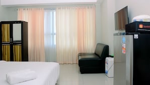A hotel room with a bed, a chair, a television, and a refrigerator. - Fully Furnished With Comfortable Design Studio Springlake Summarecon Apartment (Bekasi)