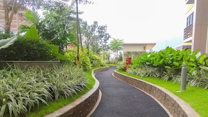 A curved pathway flanked by lush greenery and a brick wall, leading to a building with a visible entrance. - Fully Furnished With Comfortable Design Studio Springlake Summarecon Apartment (Bekasi)