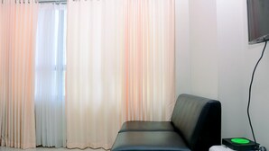 A room with a black leather sofa, a white radiator, and a television mounted on the wall. - Fully Furnished With Comfortable Design Studio Springlake Summarecon Apartment (Bekasi)