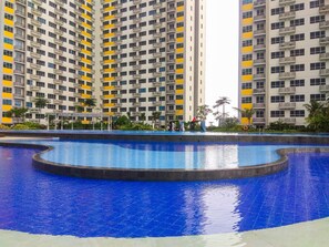 A large swimming pool with a curved design, surrounded by high-rise residential buildings with balconies. - Fully Furnished With Comfortable Design Studio Springlake Summarecon Apartment (Bekasi)