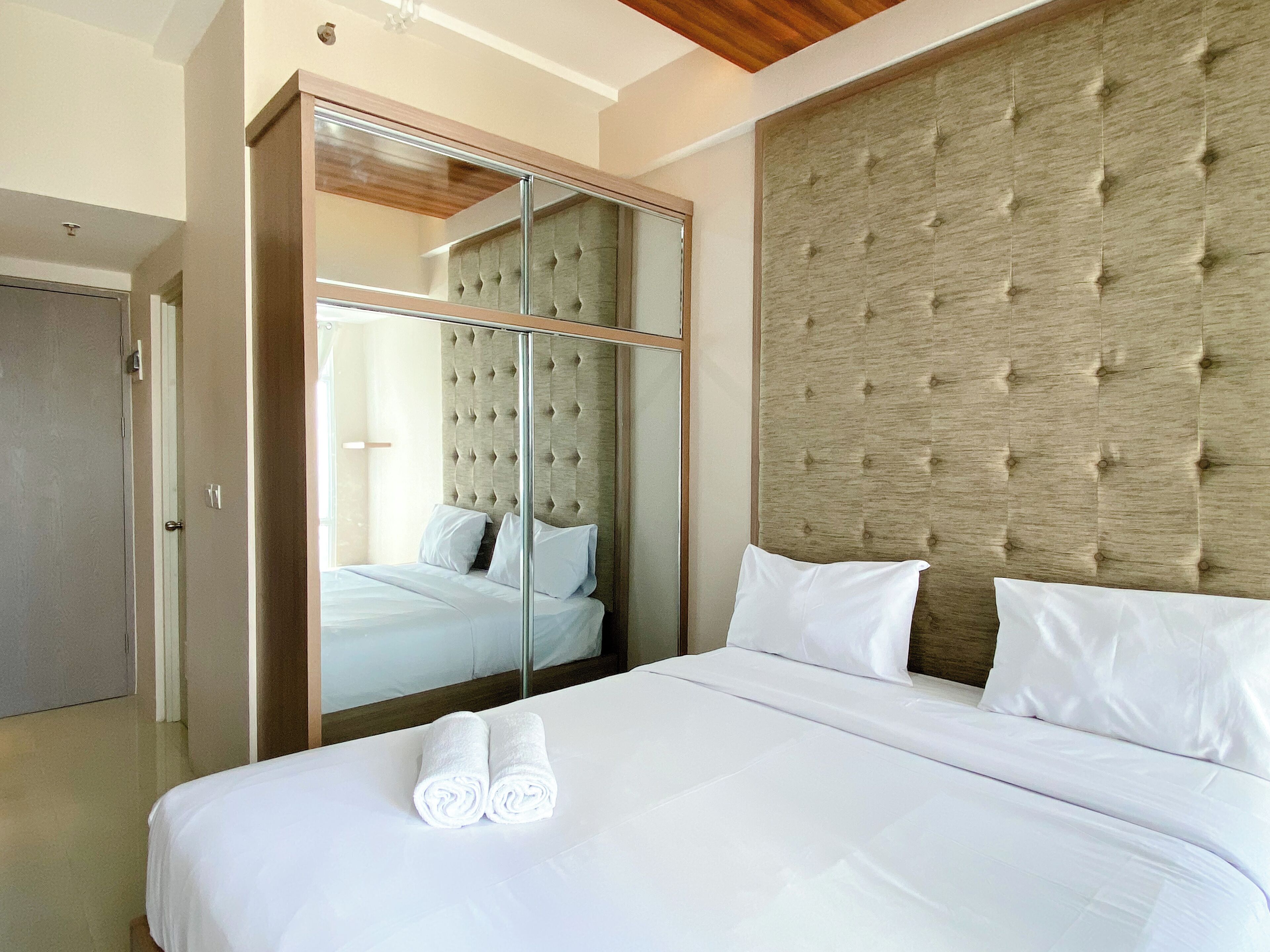 A hotel room with a large bed, a mirrored wardrobe, and a tufted headboard.