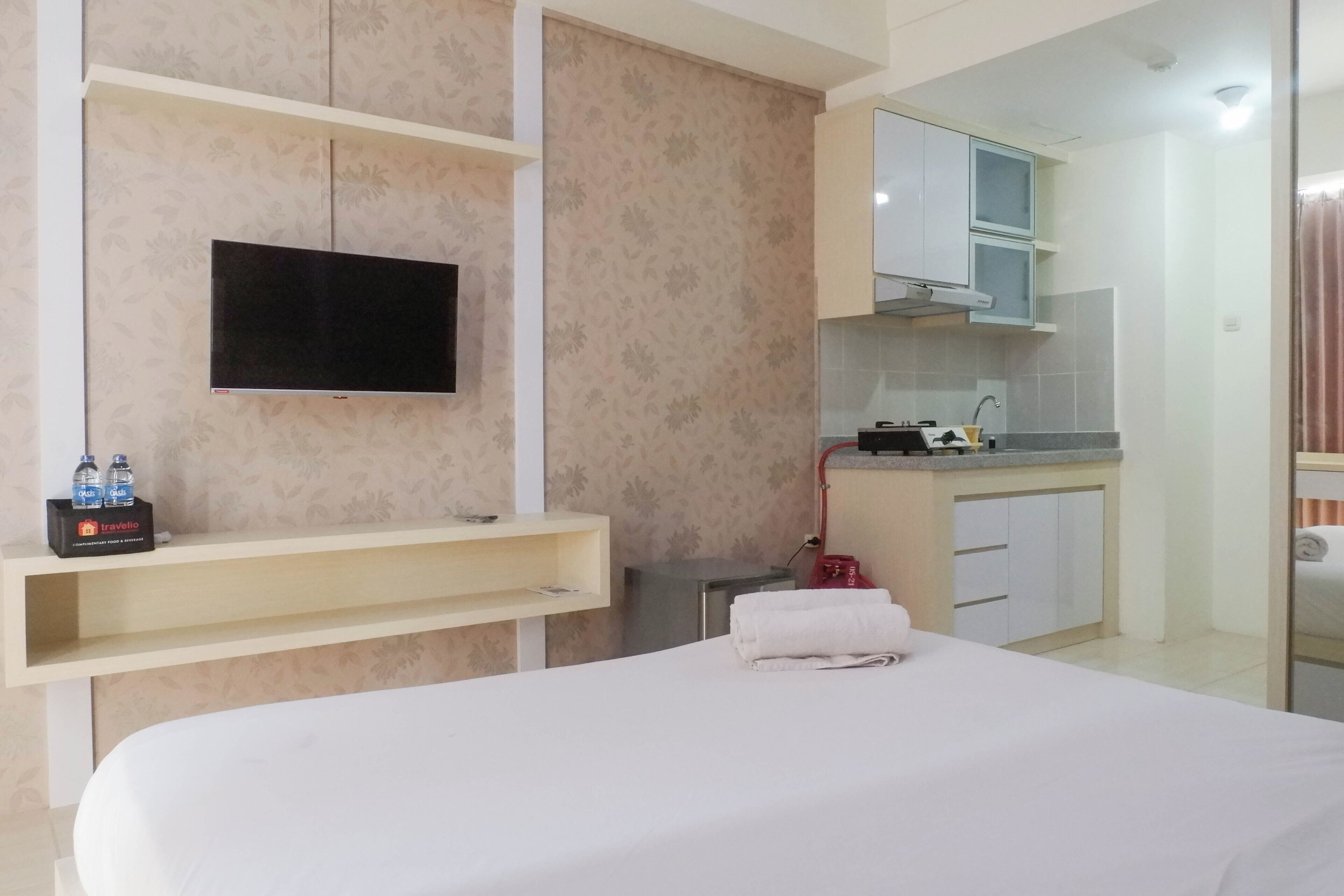 Ein Hotelzimmer mit Bett, einem an der Wand montierten Fernseher, einer kleinen Küchenzeile und einem durchgegangenen Badezimmer.