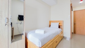 Une chambre avec un lit en bois, un matelas blanc et une tête de lit en bois. On y trouve une armoire en bois avec un miroir, ainsi qu’une petite table en bois accompagnée d’une chaise.