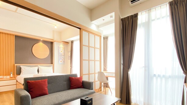 A modern hotel room with a sofa, a small table, a bed, and a large window with curtains. - Best Homey 1Br At 52Th Floor Vasanta Innopark Apartment (Cikarang)