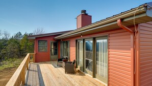 Ein rotes Haus mit einer Holzterrasse, großen Schiebeglastüren und einem Schornstein.