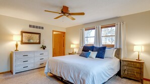 Ein Schlafzimmer mit einem Bett, zwei Nachttischen, einer Kommode, einem Deckenventilator und einem Fenster mit Vorhängen.