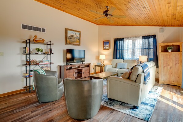 A living room with a sofa, armchairs, a TV, a wooden ceiling, and a bookshelf.