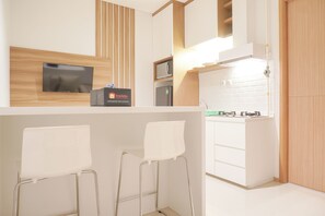 A modern kitchen with a flat-screen TV, a microwave, and a refrigerator. There are two white bar stools and a travelello sign. - Nice And Comfort 1Br At 25Th Floor Samara Suites Apartment (Jakarta)