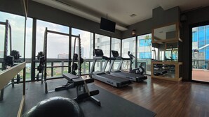 A modern gym with treadmills, weight machines, and a large window offering a city view. - Nice And Comfort 1Br At 25Th Floor Samara Suites Apartment (Jakarta)