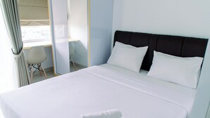 A neatly made bed with white linens and two rolled towels, a dark headboard, and a chair in the background. - Nice And Comfort Studio At Serpong Garden Apartment (Cisauk)
