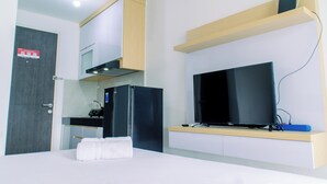 A modern hotel room with a kitchenette, a flat-screen TV, a towel on the bed, and a door with a sign. - Nice And Comfort Studio At Serpong Garden Apartment (Cisauk)