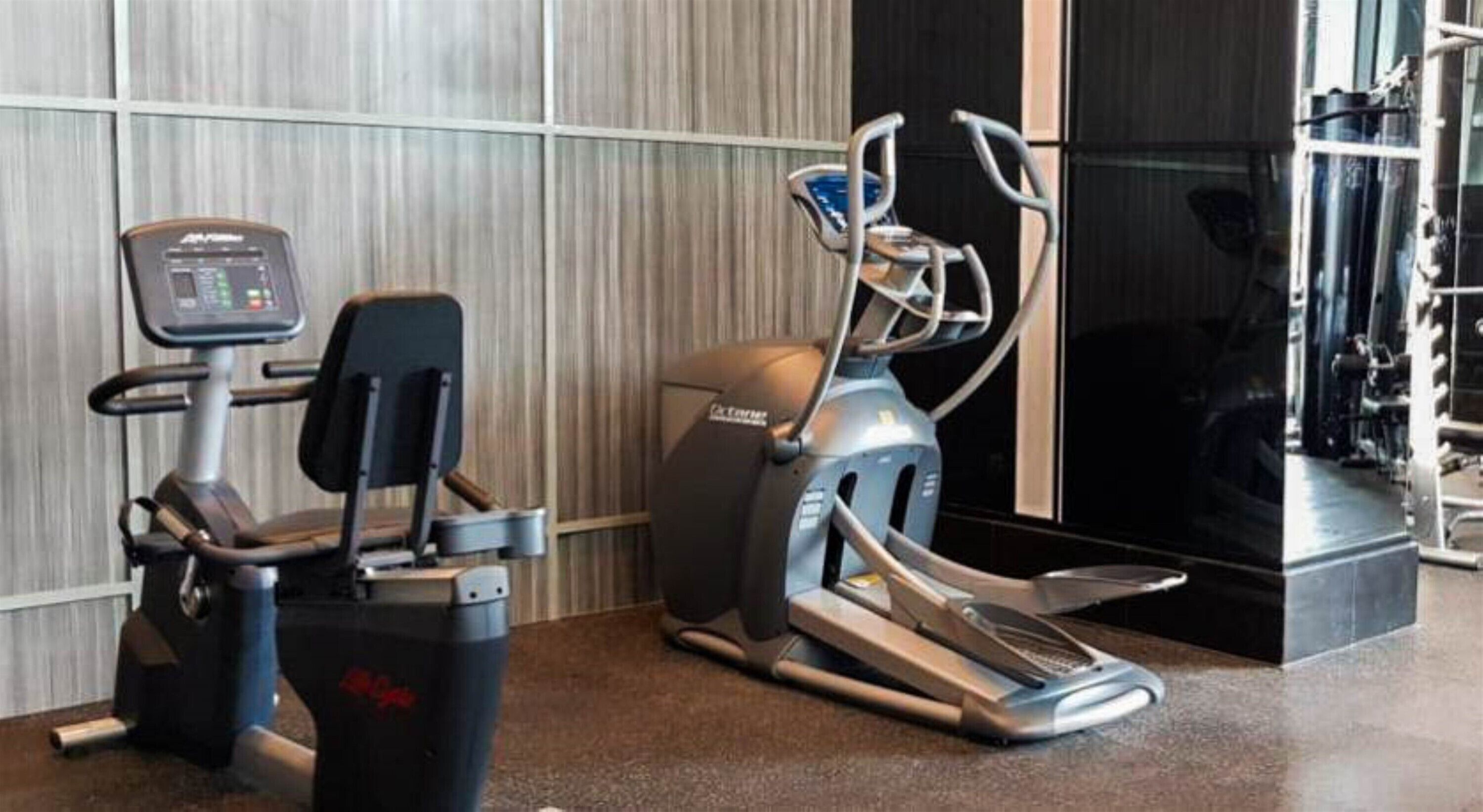 A gym with cardio machines, including a treadmill and an elliptical, against a wall with a striped pattern.