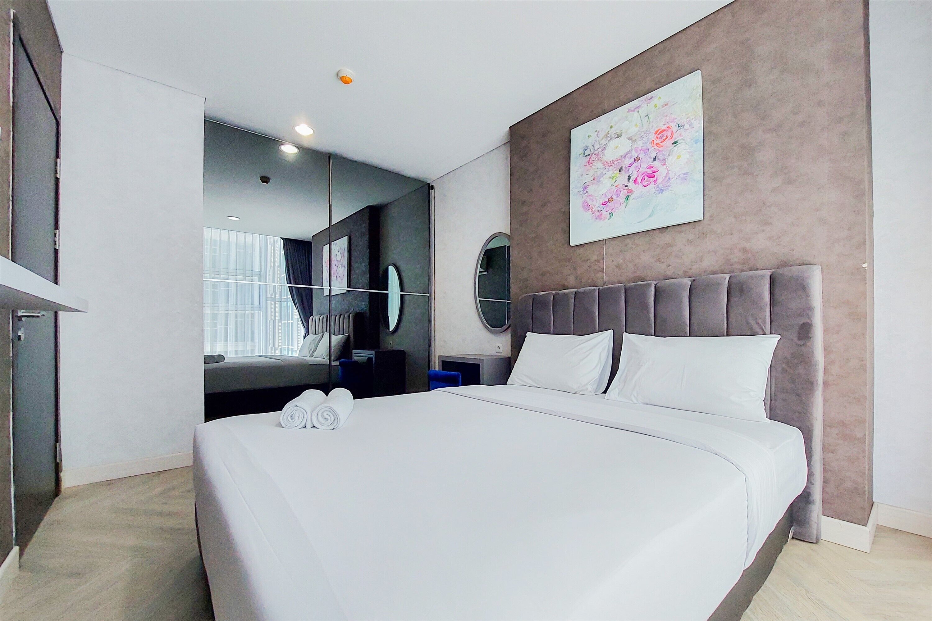 A modern hotel room with a large bed, a mirror, a painting, and a view of the city.