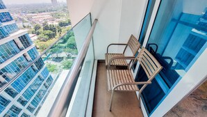 A balcony with two wooden chairs, a metal railing, and a view of a cityscape with modern buildings and greenery. - Nice And Homey 1Br At Brooklyn Alam Sutera Apartment (South Tangerang)
