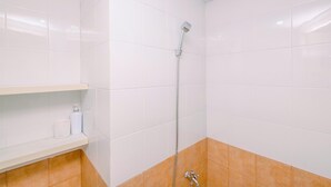 A bathroom with white tiles, a shower, a shelf with toiletries, and a brown-tiled lower section. - Fancy And Nice Studio (No Kitchen) At Green Pramuka City Apartment (Jakarta)