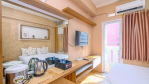 A hotel room with a bed, a TV, a wooden desk with a kettle and water bottles, and a window with curtains. - Fancy And Nice Studio (No Kitchen) At Green Pramuka City Apartment (Jakarta)