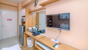 A hotel room with a wooden desk, a microwave, a refrigerator, a TV, and a plant on the wall. - Fancy And Nice Studio (No Kitchen) At Green Pramuka City Apartment (Jakarta)