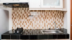 A kitchen with a black countertop, a stainless steel sink, and a white cabinet above the sink. - Strategic And Comfy Studio Apartment At Margonda Residence 5 (Depok)