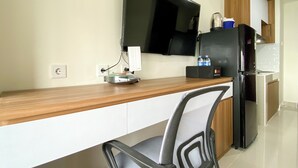 A kitchen with a wooden countertop, a black chair, a refrigerator, and a flat-screen TV mounted on the wall.