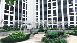 A modern building with a white facade and multiple windows. There are green plants and a white metal structure in the foreground.
